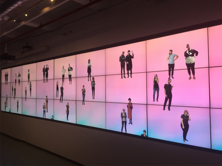 A digital art display depicting cut outs of people on a pink, yellow and blue gradient background.