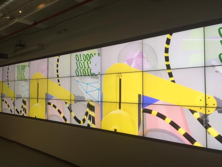 digital exhibition on a large screen grid depiction yellow machines, wireframe figures and binary code.