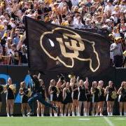 Student runs down sideline with a giant CU flag during a football game